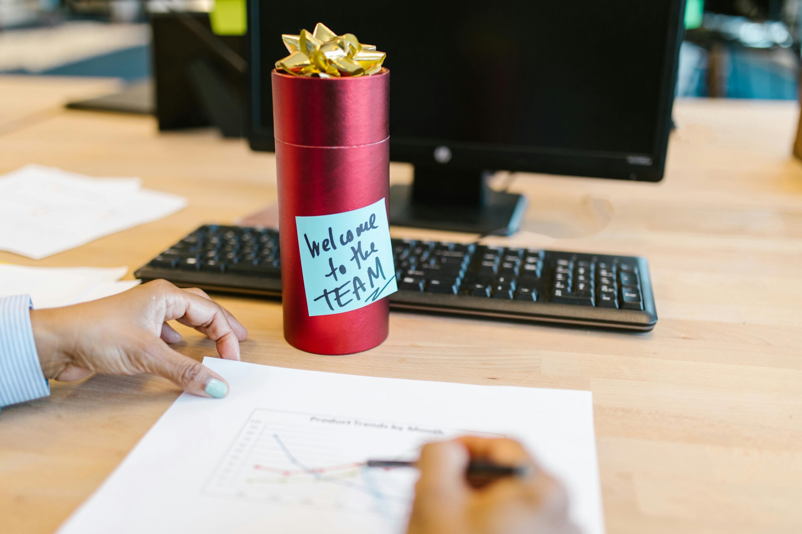 A welcoming gift on an office desk with a computer and person holding a chart.